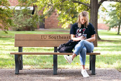 Student on mobile phone sitting on a bench on the IU Southeast campus.